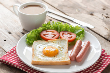 Fried toast with egg, sausage and a cup coffee on wood table.