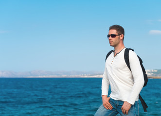 Male tourist with backpack standing near the sea.