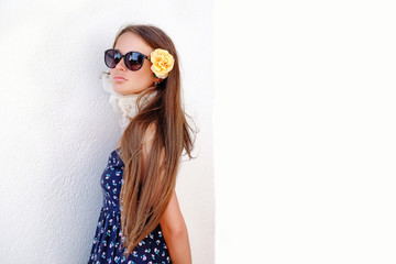 Girl model in a hat and sunglasses posing against a white wall.