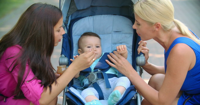 Two moms feeding baby boy infant food 