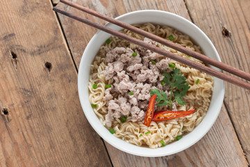 Noodles with minced pork in white bowl on wood table. Top view.