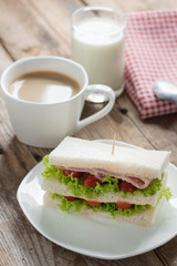 Sandwich ham with cheese, coffee and milk on wood table.