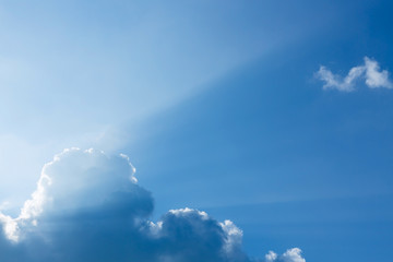 light rays of sun beam through clouds in clear blue sky