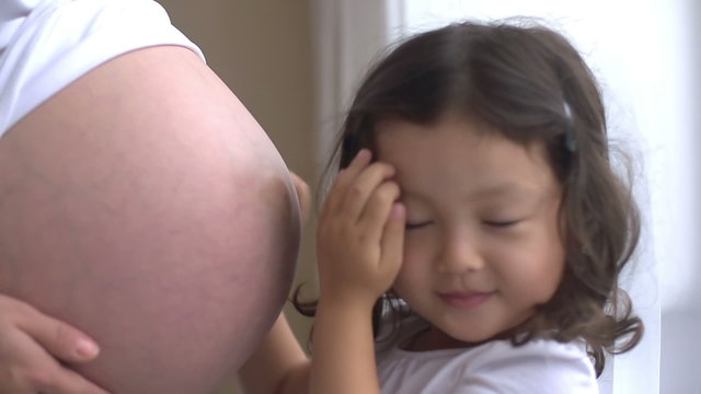 Curious little girl listening to her pregnant mother's belly,dolly shot, slow motion