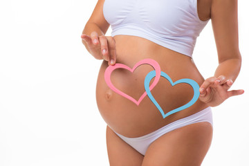 Happy pregnancy. Smiling pregnant woman holding a plate with two hearts. Mother Love. Twins, girl, boy.
