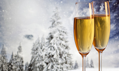 Two champagne glasses and snowy fir trees in the background