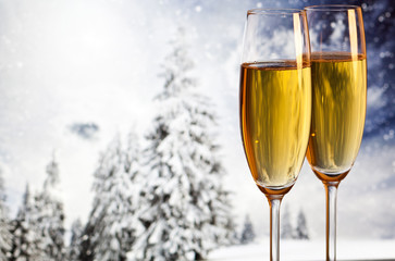 Two champagne glasses and snowy fir trees in the background