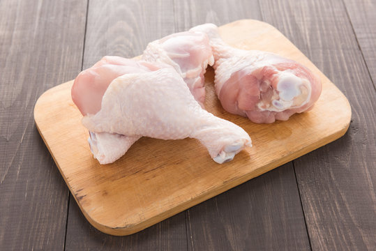 Raw chicken drumsticks on cutting board on wood table