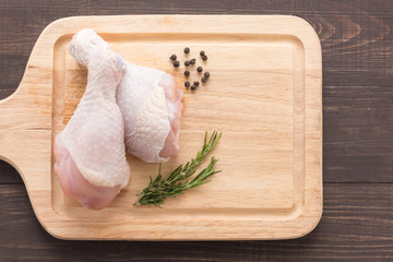 Raw chicken drumsticks on cutting board on wooden background