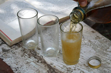 three glasses in which is poured beer from a big glass bottle


