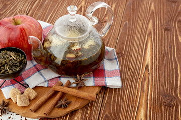 Ripe apple, cinnamon and fruit drink in glass teapot on wooden background