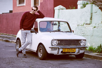 Handsome man leaning against a classic little car in a city stre