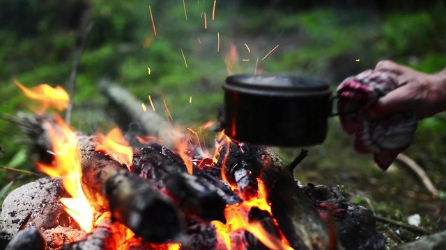 Cooking coffee on a campfire in the foggy forest. Coffee is boiling on the bonfire in the small pot. Green background.