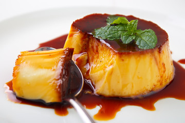Caramel custard pudding and spoon on plate with lemon balm leave on top - 94498415