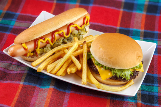 Hot dog , french fries and cheese burger on plate , fast food lunch on red fabric surface