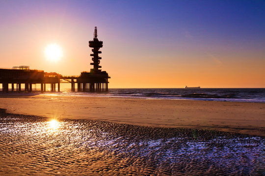 Evening silhouette of the pier of Scheveningen, the Netherlands, with ripples in the sand and water on the beach