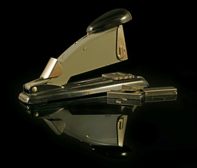 Old metal stapler on black background