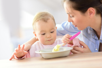 Baby girl eating lunch with help of her mommy