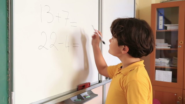 Little schoolboy solving mathematic problem on the blackboard