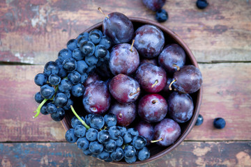 Plums and grapes in a bowl on the wooden table 
