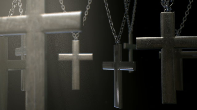 An extreme closeup pan across a group of metal crucifixes hanging from chains on a dark dramatically lit background