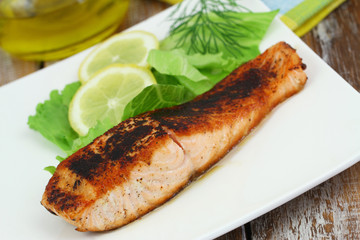 Grilled salmon steak with green salad and lemon on white plate
