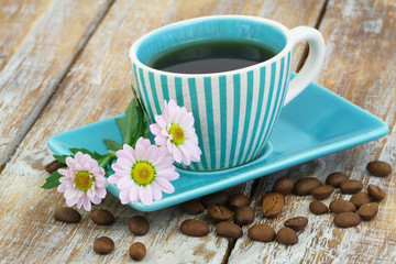 Cup of coffee and pink daisy flowers on rustic wooden surface
