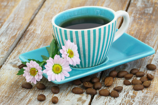 Cup of coffee and pink daisy flowers on rustic wooden surface
