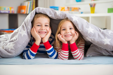 Two happy children lying under blanket - Powered by Adobe