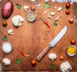Fototapeta na wymiar Concert vegetarian food Potato onion cauliflower garlic cherry tomatoes mushrooms seasoning hot red pepper and knife frame with space for text on rusti? wooden background top view