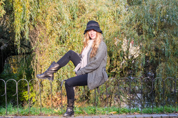 The young beautiful girl walks in the autumn park among yellow leaves in a coat on a sunny day