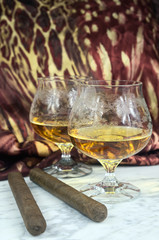 Two glasses of cognac with a cigar on a marble table