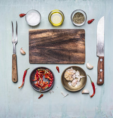 Ingredients for cooking cutting board, fork and knife for meat, hot red pepper in the bowl of garlic butter and seasonings on rustic wooden background top view