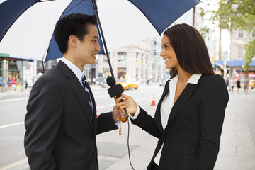 A woman with a microphone interviews a well dressed man. Could be a politician, businessman etc.
