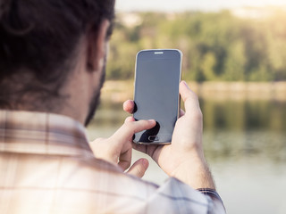 Rear view of a young man holding and using mobile smartphone