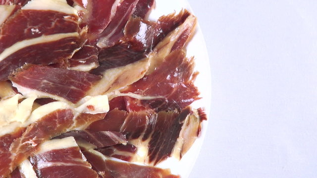aerial top view of pile of typical spanish iberico ham sliced on dish rotating spinning on white background
