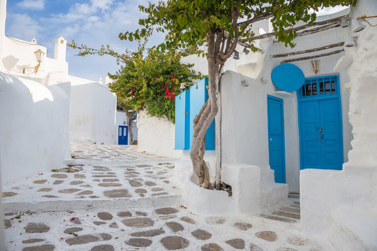 Fototapeta Mykonos tradycyjny biały streetview z niebieskimi drzwiami i drzewami, Grecja