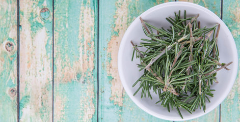 Fresh rosemary herbs over in white bowl over wooden background