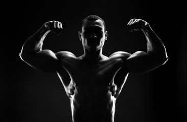 bodybuilder demonstrates biceps on a dark background