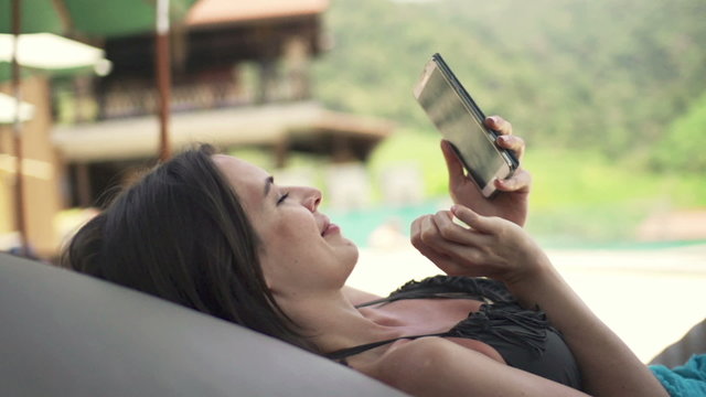 Young woman using smartphone on sunbed by pool
