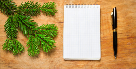 Pen and Notepad on old rustic table decorated with a fir branch.