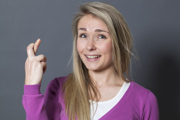 joyful blond girl trusting faith in crossing her fingers tight