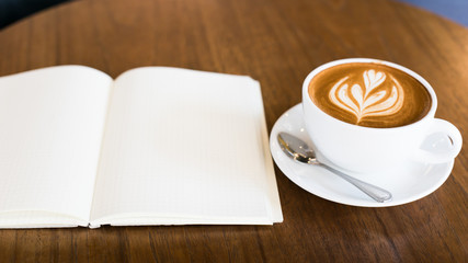 Hot latte art coffee cup on wooden table and note book, vintage