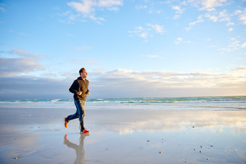 Fototapeta na wymiar Young man running along the beach at sunrise