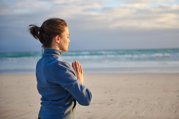 Woman with her eyes closed and hands together on the beach