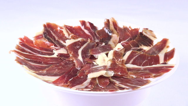 view of pile of typical spanish iberico ham sliced on dish rotating spinning on white background
