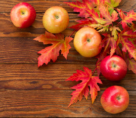red apples and colorful autumn leaves of maple on a wooden backg