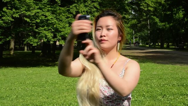 young attractive happy asian woman shoots herself in the park - selfie 