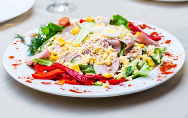 green salad with ham, egg, corn and pepper on the white tableclo