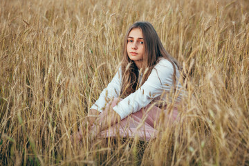 Naklejka na ściany i meble Young woman wearing dress sitting in field with wheat